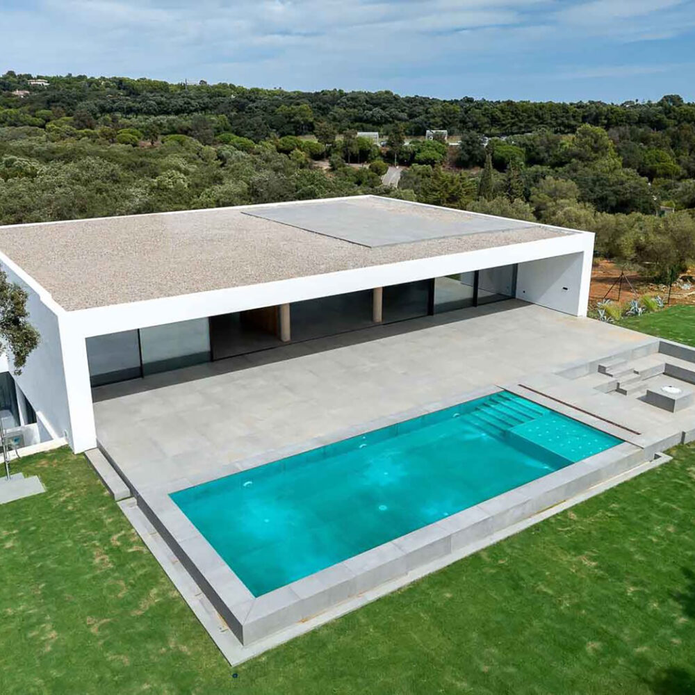 Vista aérea de la moderna Villa 93 con piscina, jardín y paisaje boscoso en Sotogrande.
