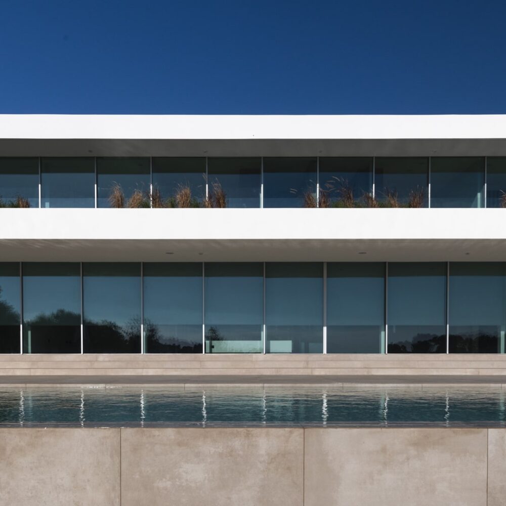 Modern two-story villa with large glass windows, a planted balcony, and an infinity pool.