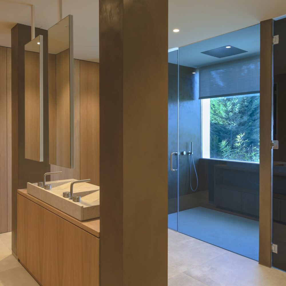 A contemporary Cork Oak Mansion bathroom with light wood cabinets, stone sink, and glass shower.