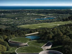 Aerial view of circular luxury villas with green roofs, a golf course, lake, and ocean near Sotogrande.