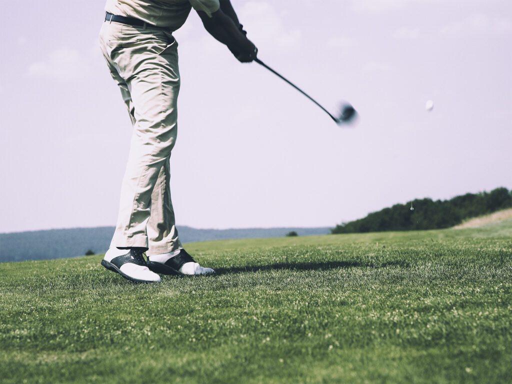 A golfer in beige trousers and golf shoes swinging a club on a lush green golf course in Marbella.