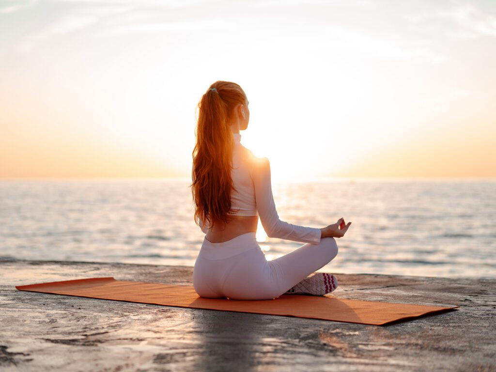 Woman meditating on a yoga mat by the sea at sunrise, reflecting the peaceful lifestyle in Marbella.